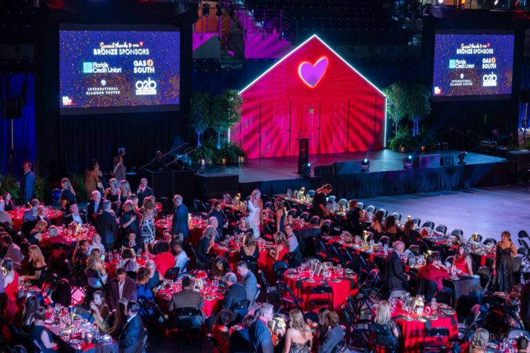 Guests at red-draped dinner tables facing the red house stage at the Red Shoe Affair