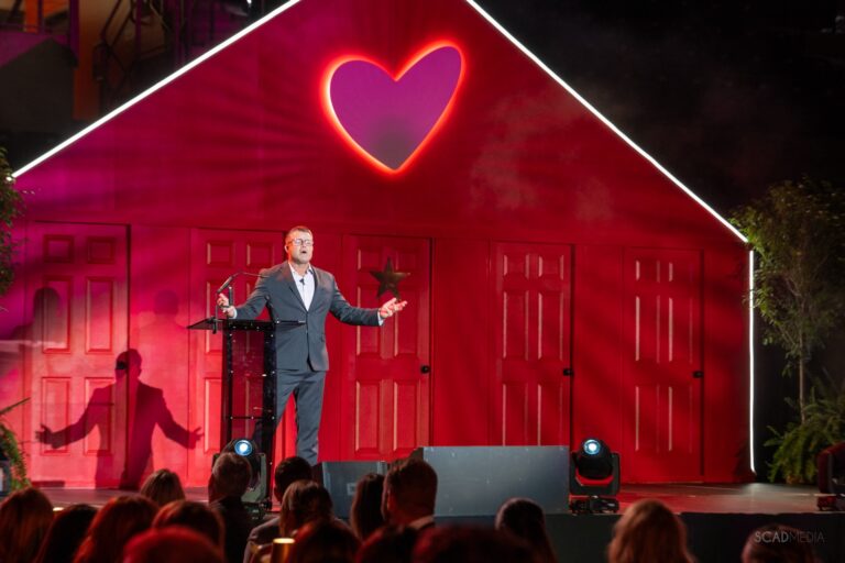 Speaker on stage in front of the glowing heart house set